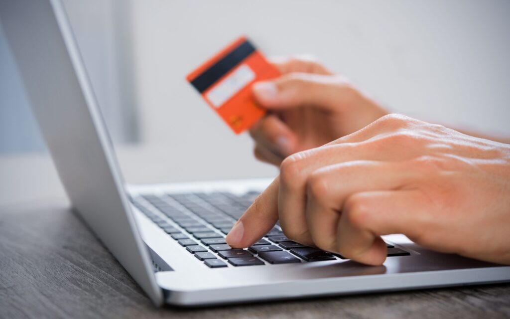 picture of a man typing on a laptop, holding a debit card